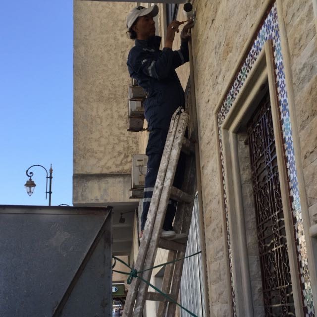 Pose d'un luminaire en façade depuis une échelle dans la médina