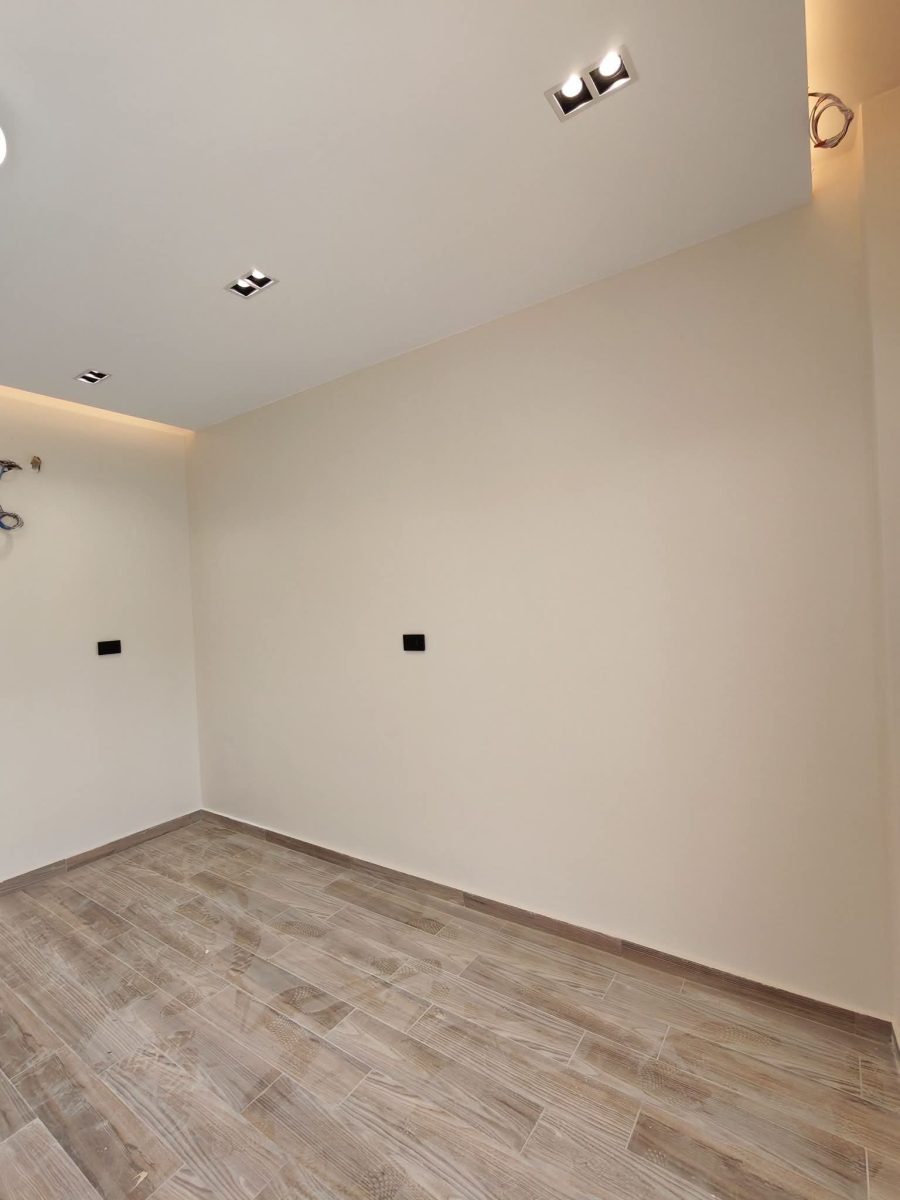 Pièce aux murs peints crème avec faux plafond à spots et sol effet bois