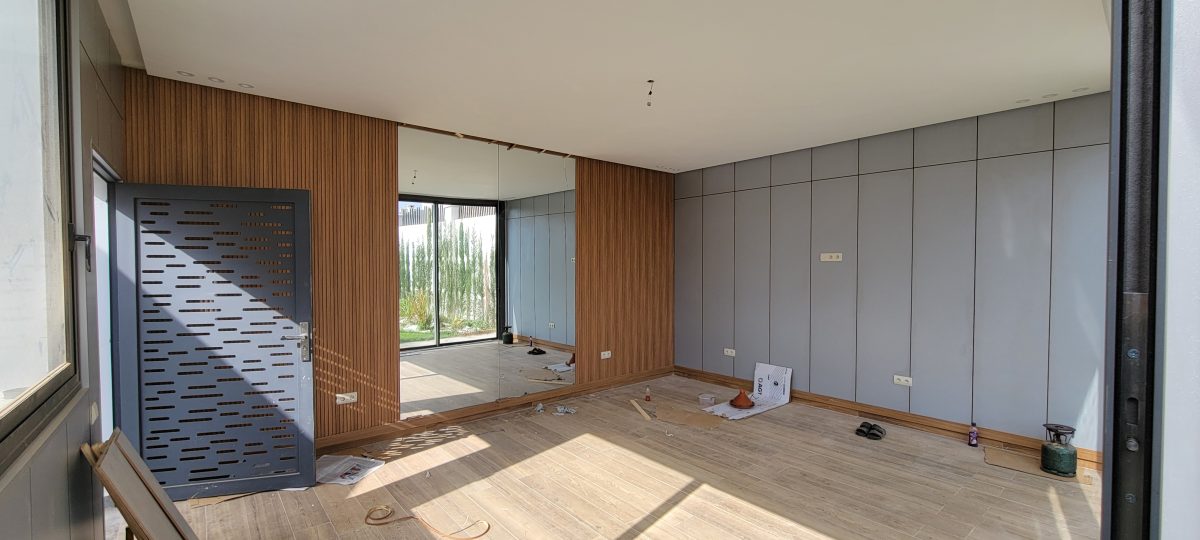 Séjour avec habillage mural en tasseaux de bois et porte en aluminium perforé