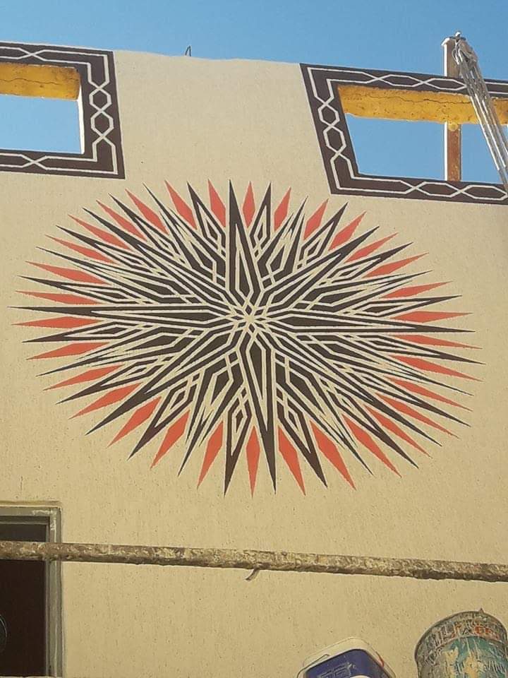 Grande rosace géométrique peinte sur une façade beige
