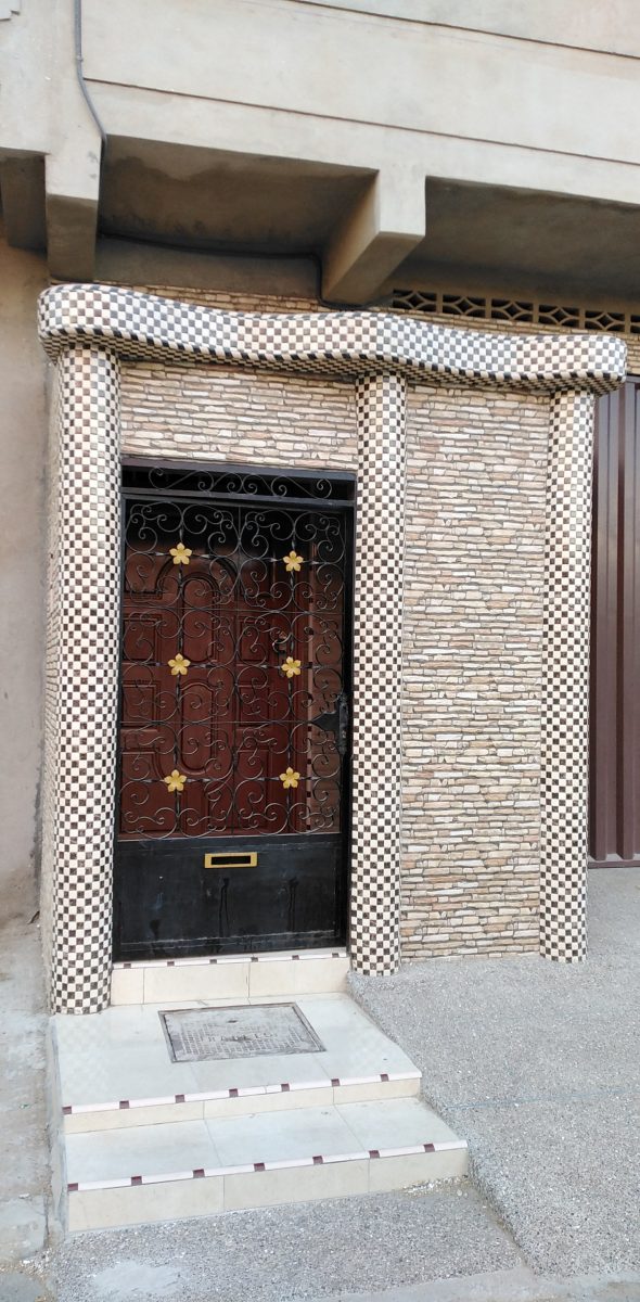 Encadrement d'entrée en carrelage mosaïque damier et pierre, porte en fer forgé