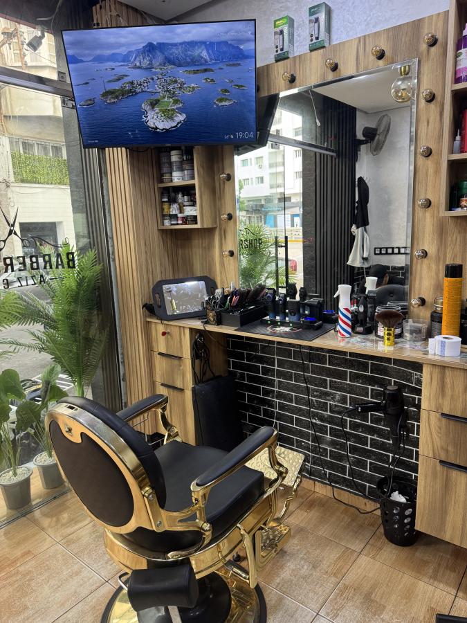 Poste de barbier avec fauteuil noir et doré, miroir à ampoules et mur en brique