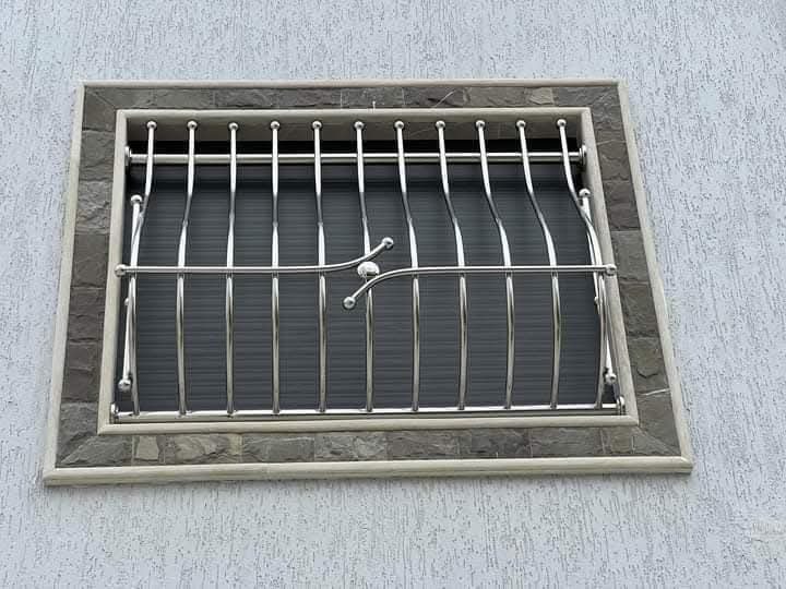 Grille de défense de fenêtre en inox poli à barreaux cintrés, sur encadrement en pierre