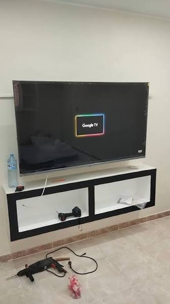Téléviseur fixé au mur avec meuble TV suspendu, installation en cours