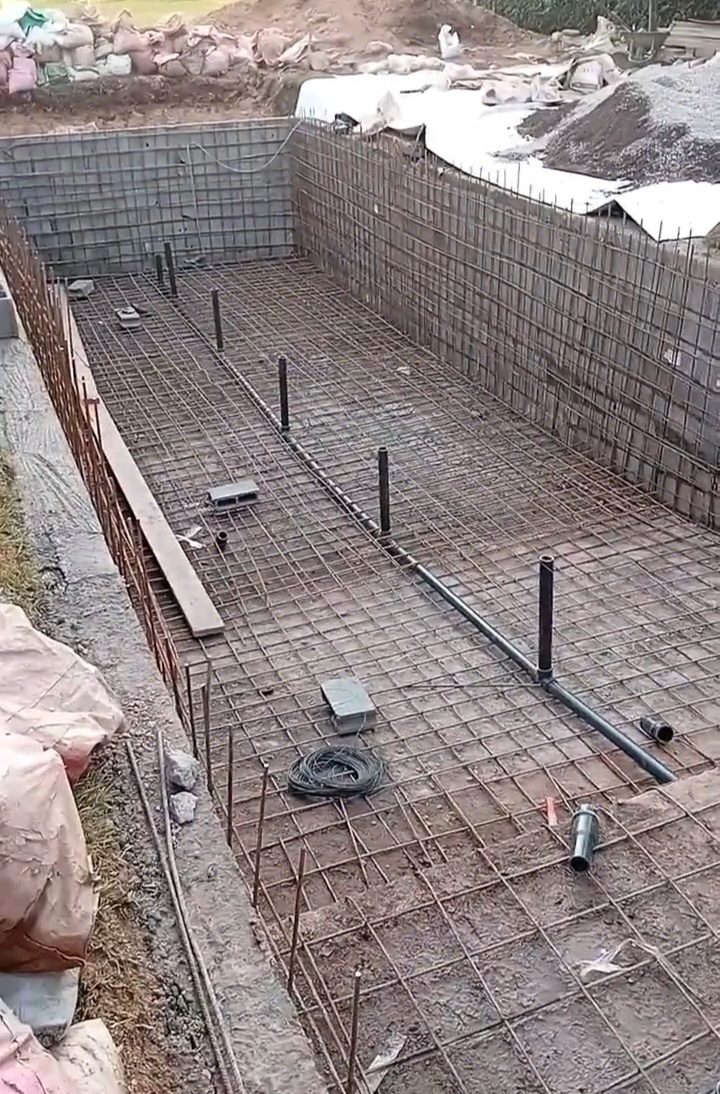 Chantier de bassin en béton armé avec ferraillage et réseau de plomberie PVC