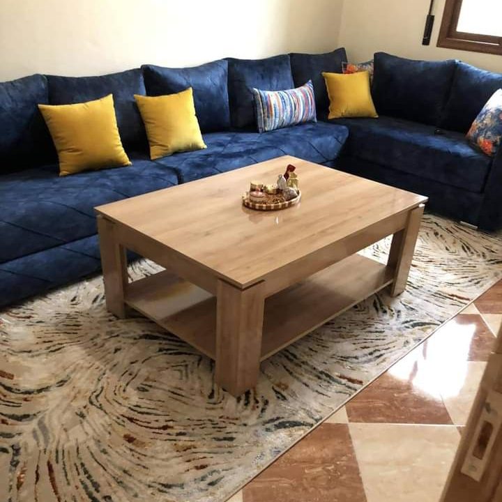 Table basse carrée en bois clair devant un canapé d'angle bleu