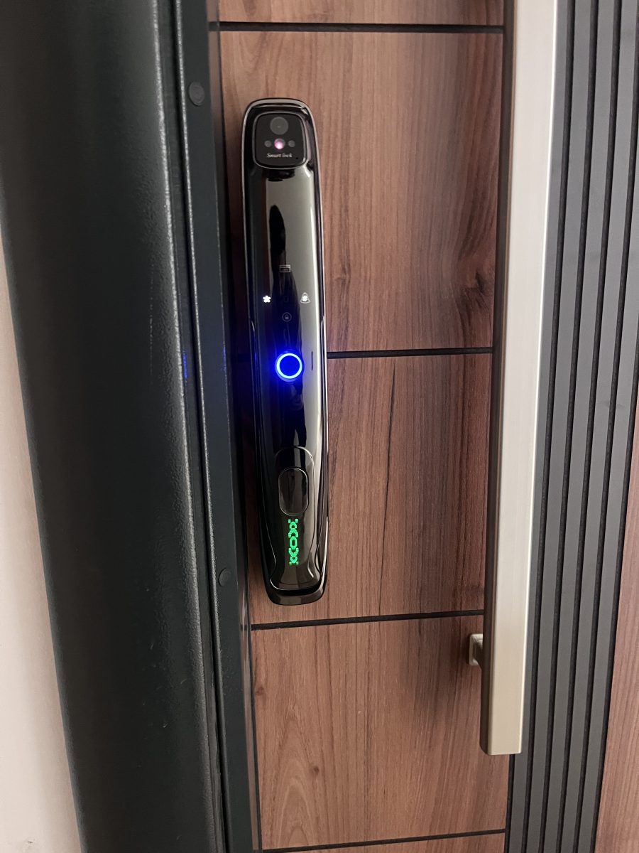 Serrure connectée noire à caméra sur une porte effet bois