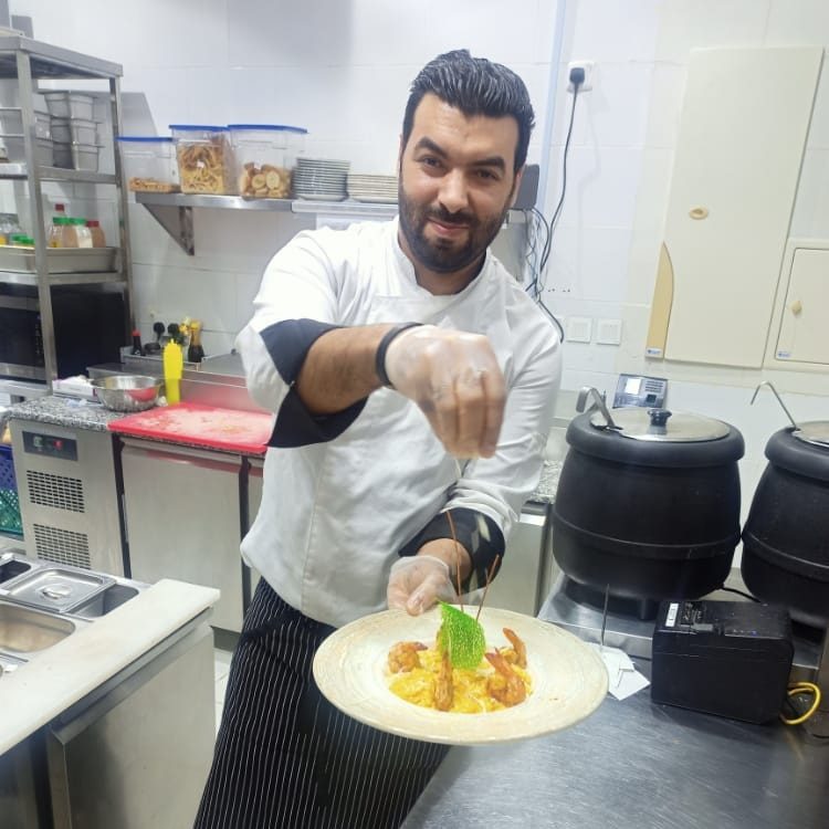 Cuisinier présentant une assiette de crevettes et riz en cuisine pro