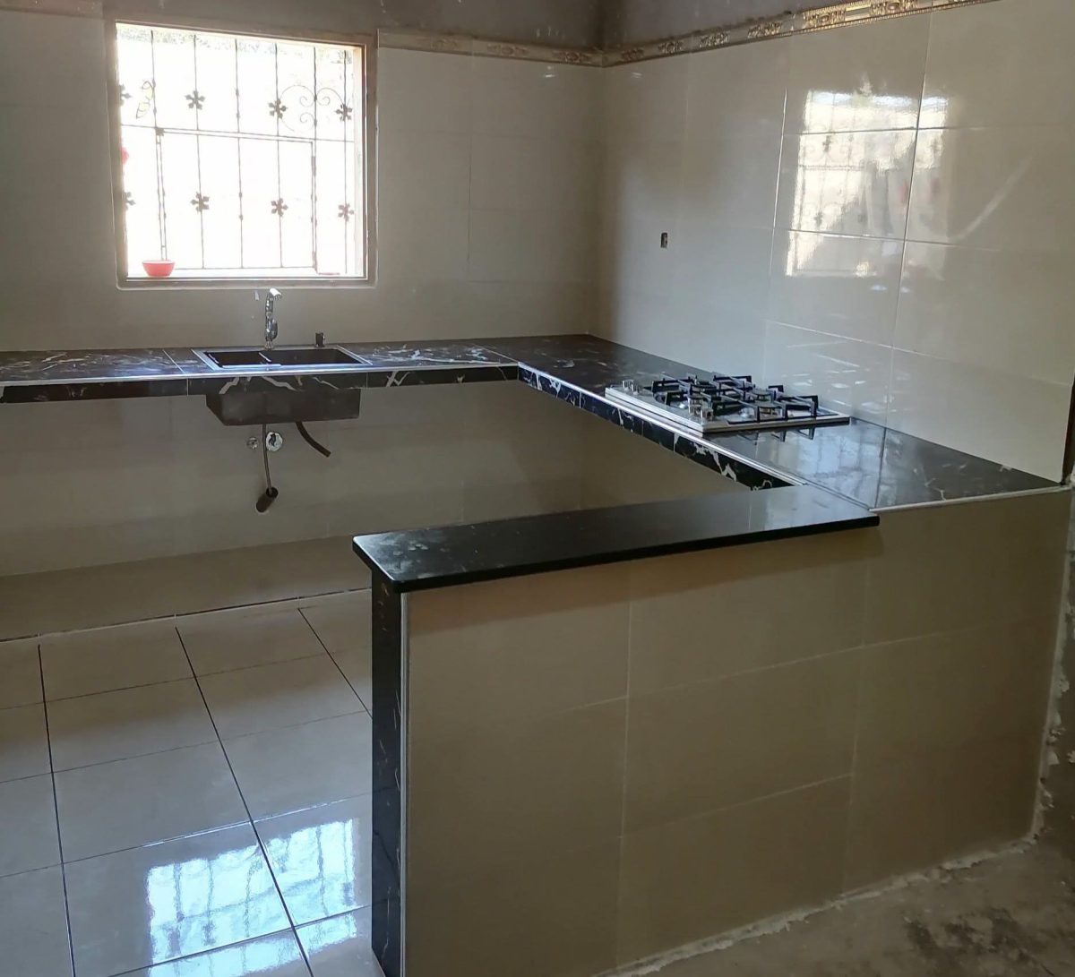 Cuisine en U en faïence beige avec plan en granit noir et évier