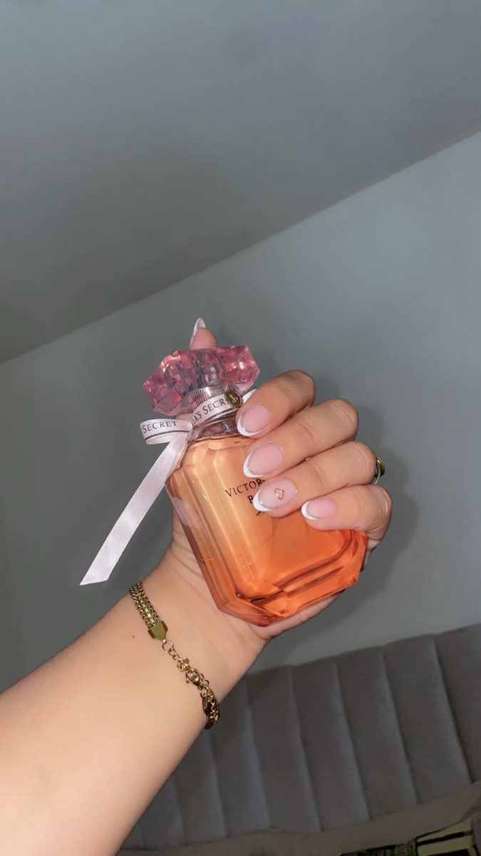 Main aux ongles en French manucure tenant un parfum