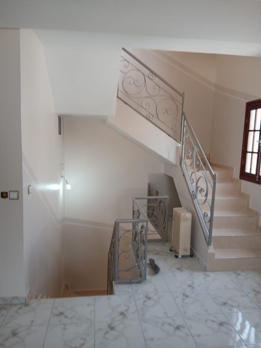 Cage d'escalier peinte beige avec garde-corps en fer forgé