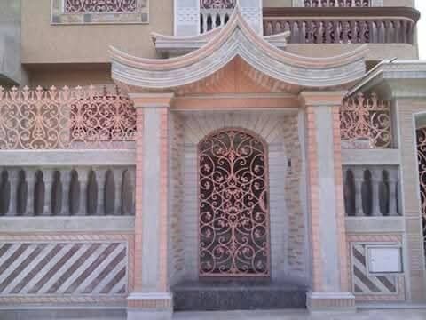 Entrée à porte en fer forgé à volutes sous auvent maçonné