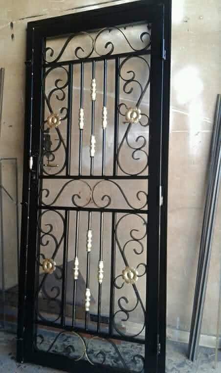 Grille de porte en fer forgé noir à volutes et fleurons dorés, en atelier