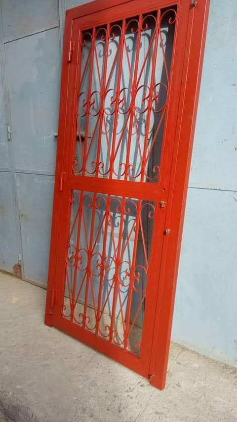Grille de porte en fer forgé laqué rouge à volutes, en atelier