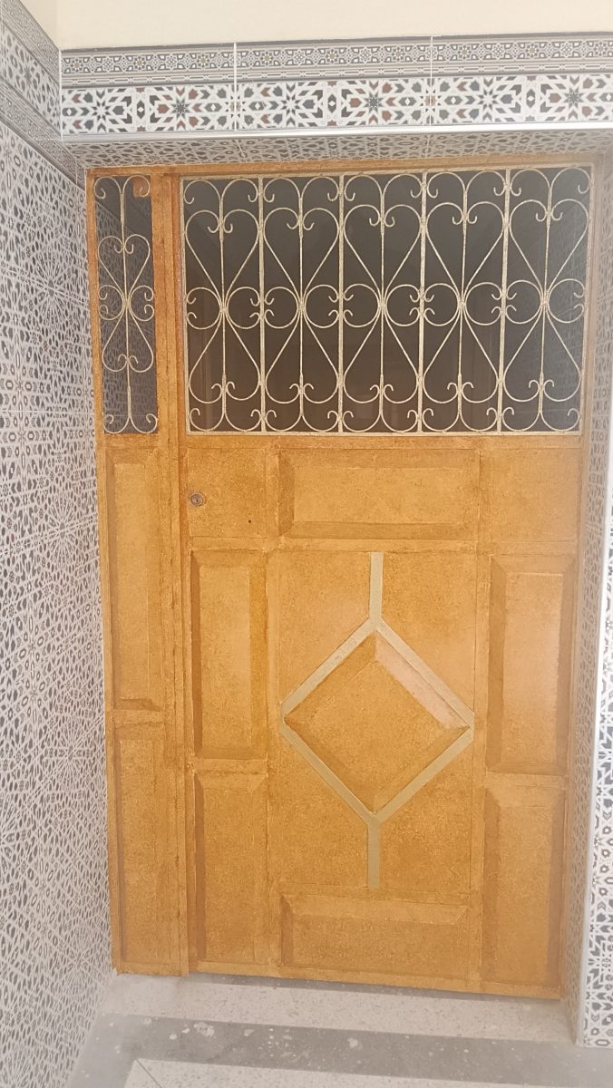 Porte en tadelakt ocre à panneaux et losange doré avec imposte fer forgé