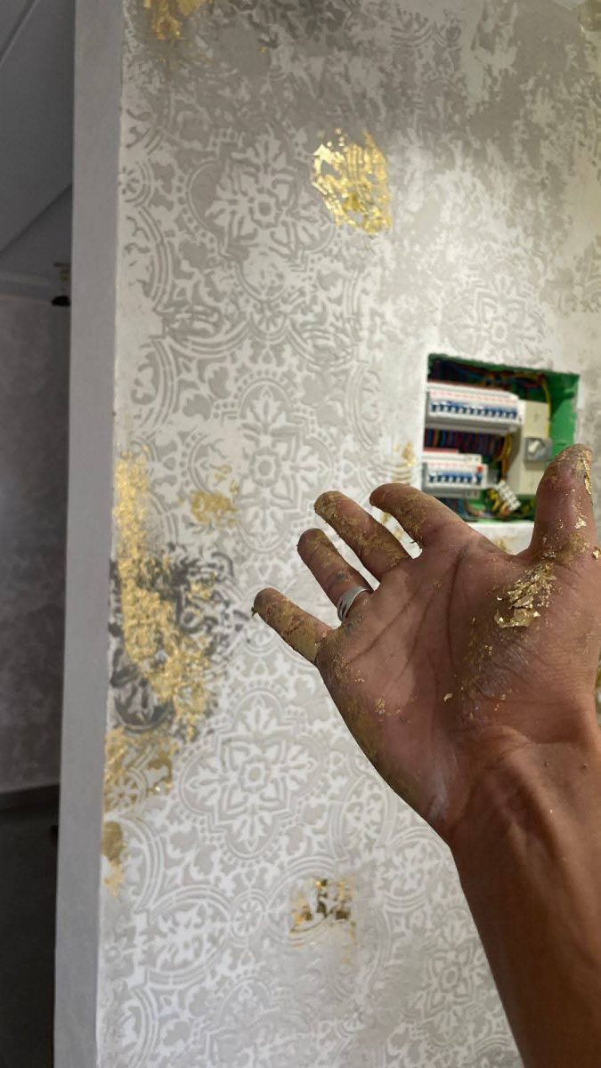 Application de feuilles d'or sur un mur damassé