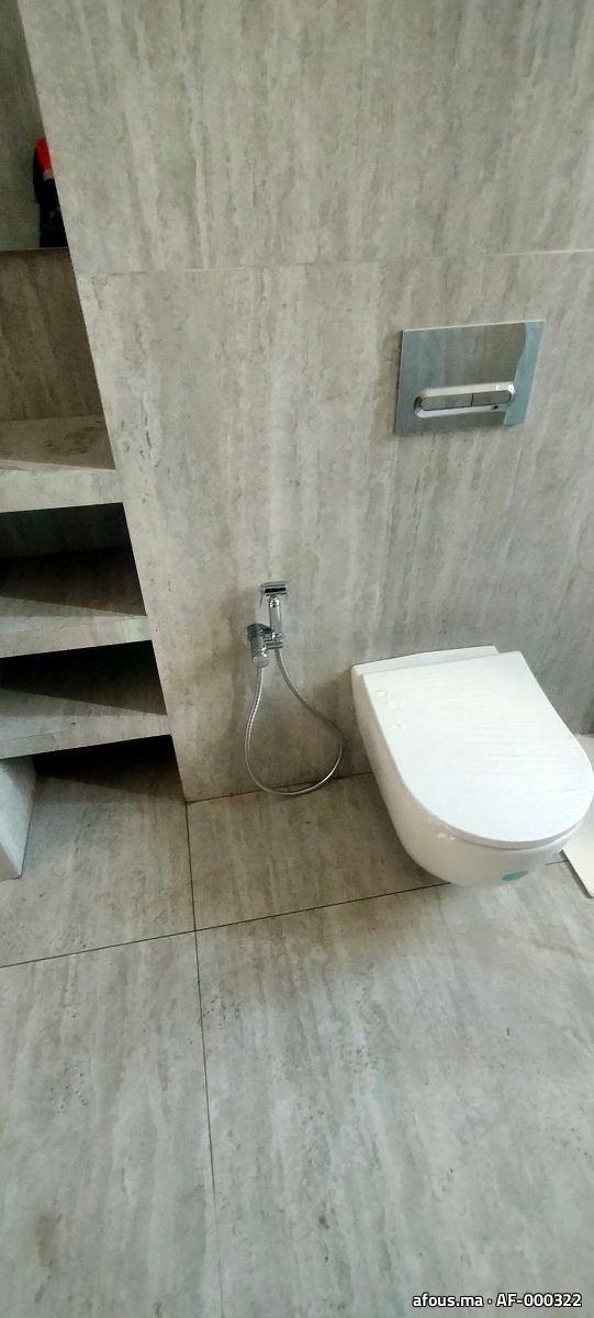 WC suspendu blanc à plaque chromée sur mur travertin — Marrakech