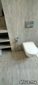 WC suspendu blanc à plaque chromée sur mur travertin — Marrakech