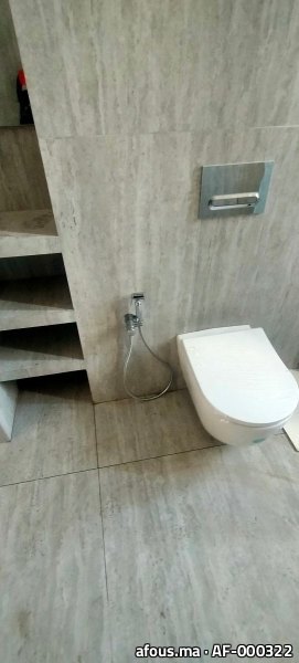 WC suspendu blanc à plaque chromée sur mur travertin