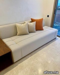 Banquette basse crème à coussins orange devant une baie — Meknès