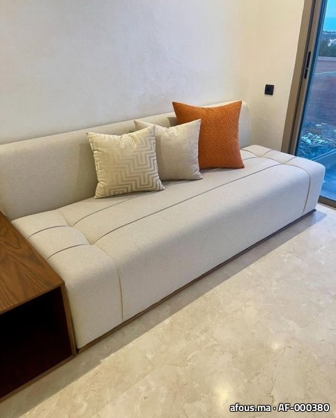 Banquette basse crème à coussins orange devant une baie