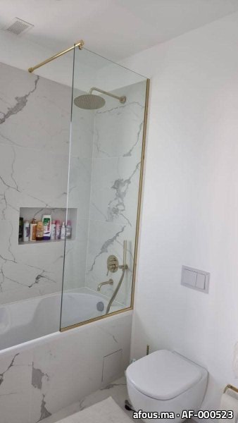 Pare-baignoire en verre à cadre laiton doré dans une salle